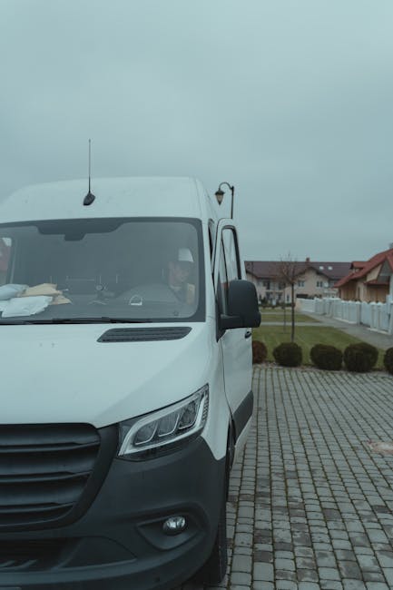 White delivery van parked in a suburban area with driver inside on a cloudy day.
